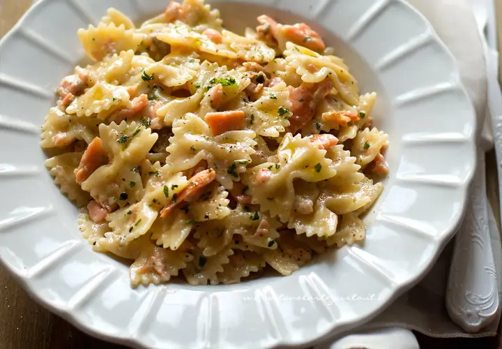 Farfalle cremose con salmone affumicato, un piatto delizioso e invitante, guarnito con prezzemolo fresco e pepe nero.