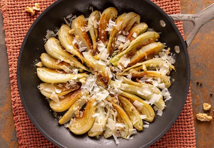 Finocchi in padella dorati, guarniti con scaglie di formaggio e noci croccanti. Un piatto semplice e saporito.