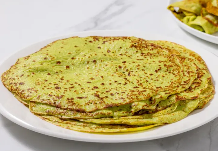 Piatto di crepes di zucchine verdi, sottili e leggermente dorate, impilate su un piatto bianco.