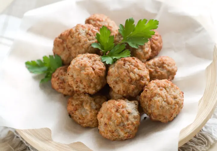 Un mucchio di polpette di pollo dorate e profumate, guarnite con prezzemolo fresco, servite su carta da forno in un piatto di legno.
