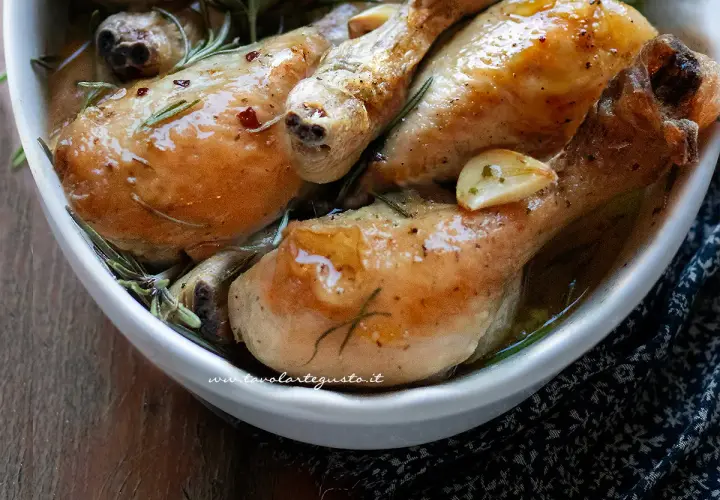 Cosce di pollo al forno succulente, dorate e profumate al rosmarino e aglio, servite in una ciotola bianca.