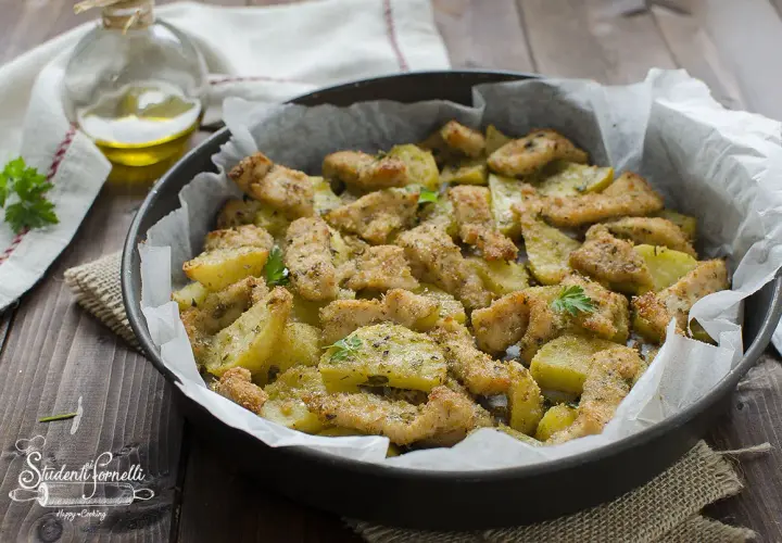 Straccetti di pollo al forno con patate, dorati e croccanti, guarniti con prezzemolo fresco.