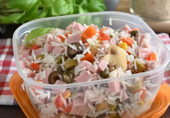 Insalata di riso colorata con prosciutto a cubetti, carote, olive, piselli e funghi, pronta per un pasto veloce.