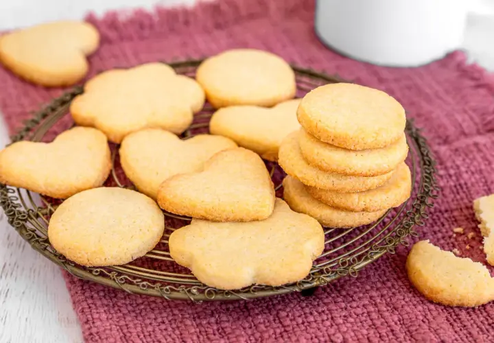 Deliziosi dolci da fare in casa: biscotti a forma di cuore e fiori su una gratella, con una pila di biscotti rotondi e un pezzo rotto in primo piano.
