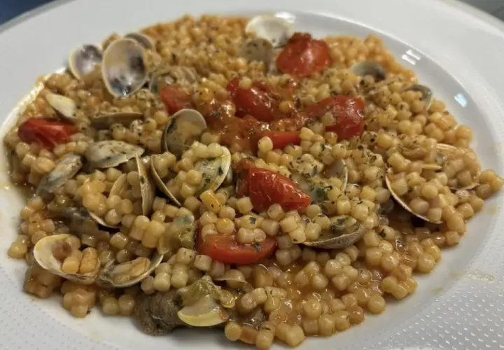 Un piatto invitante di fregola con vongole, pomodorini e prezzemolo, pronto per essere gustato.