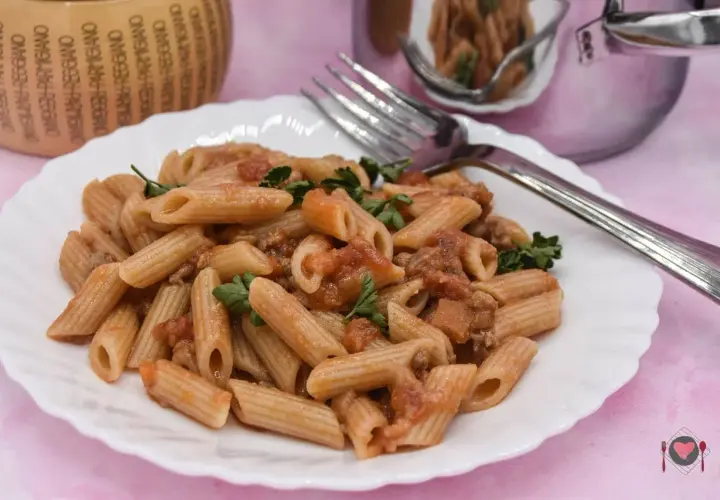 Piatto di pasta con salsiccia e pomodoro, guarnito con prezzemolo fresco. Un classico della cucina italiana, pronto per essere gustato.