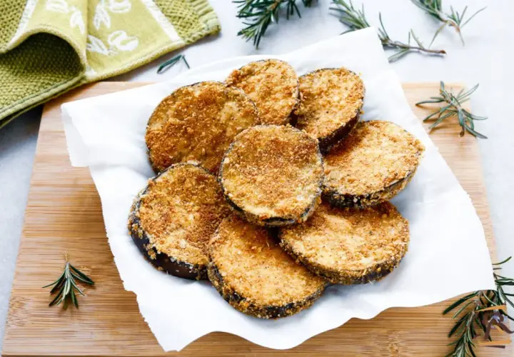 Cotolette di melanzane dorate e croccanti, servite su carta bianca con rametti di rosmarino.