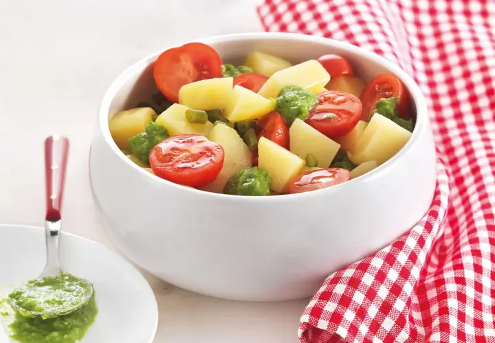 Deliziosa insalata di patate estiva con pomodorini e piselli, condita con un pesto fresco. Perfetta per un picnic o una cena leggera.