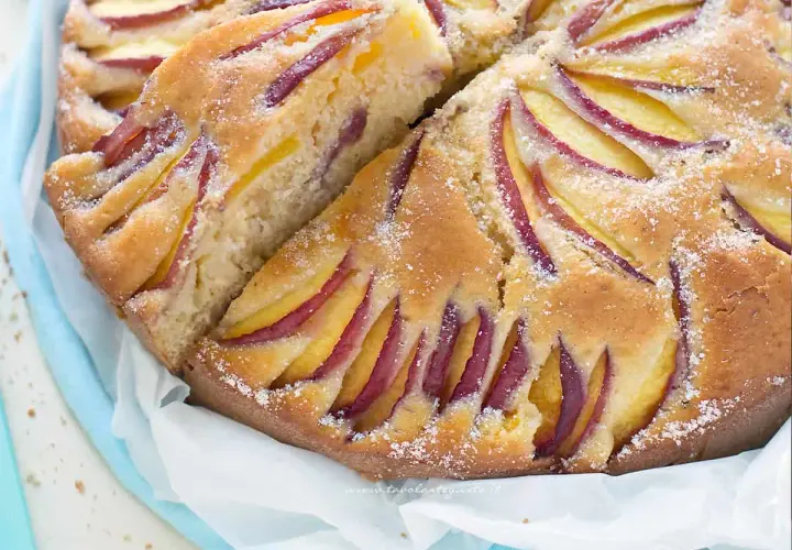 Una deliziosa torta di pesche, con fette di frutta disposte a raggiera sulla superficie dorata e cosparsa di zucchero.