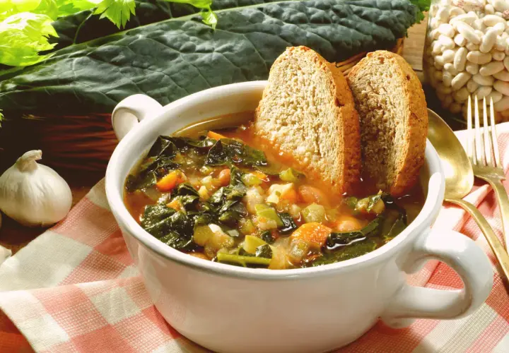 Una ciotola fumante di zuppa di cavolo nero, con pane tostato e fagioli, pronta per essere gustata.