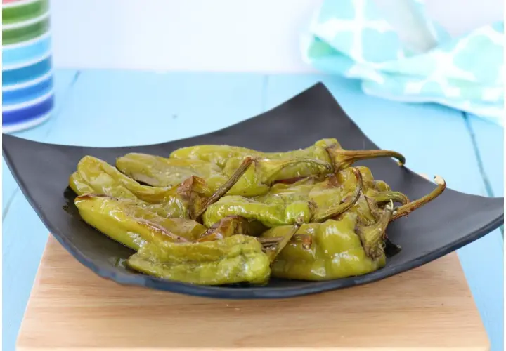 Friggitelli al forno, verdi e lucidi, serviti su un piatto nero. Un contorno saporito e facile da preparare.