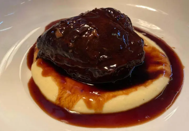 Guancia di manzo brasata, tenerissima e succulenta, adagiata su un letto di purè cremoso, il tutto avvolto da una ricca salsa scura.