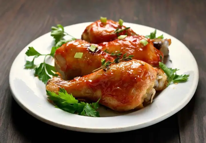 Tre cosce di pollo glassate, guarnite con prezzemolo e erbe aromatiche, pronte per essere gustate. Un delizioso pollo alla birra.