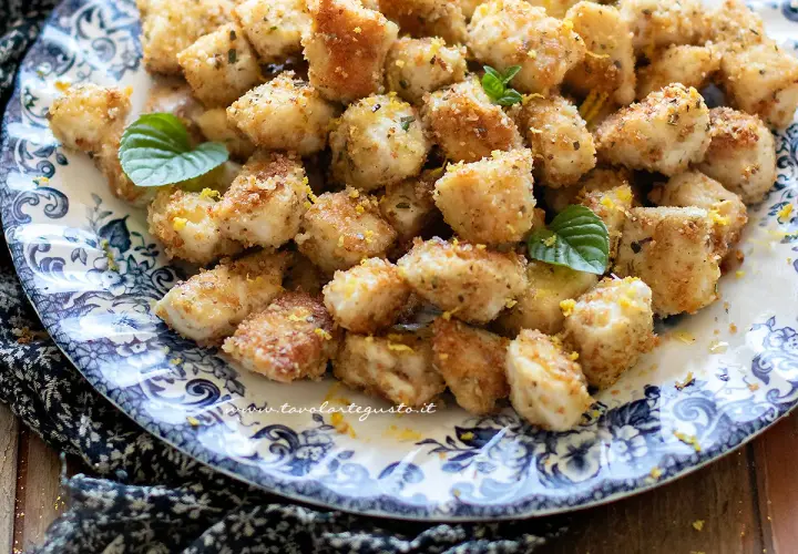 Croccante spezzatino di pollo impanato, guarnito con scorza di limone e menta fresca, servito su un piatto decorato.