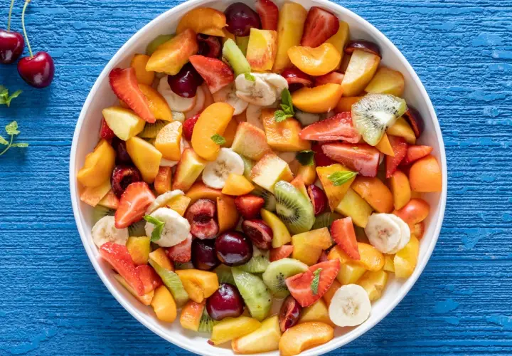 Una colorata macedonia di frutta fresca, con fragole, kiwi, pesche, banane e ciliegie, pronta per essere gustata.