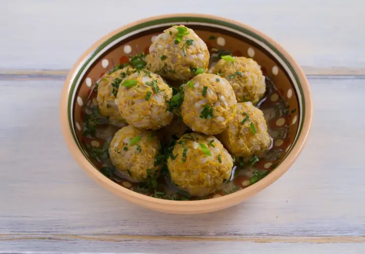 Polpette di riso avanzato, dorate e profumate, servite in una ciotola decorata, con erbe fresche tritate.