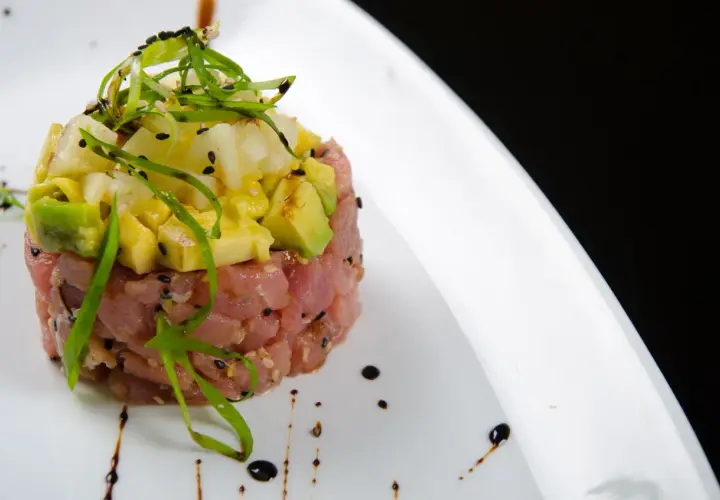 Deliziosa tartare di tonno con avocado, ananas e cipollotto fresco, guarnita con semi di sesamo e un filo di salsa.