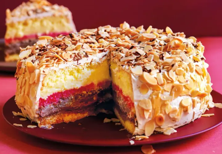 Una fetta di pizza dolce abruzzese, con strati di crema, cioccolato e confettura, ricoperta di mandorle tostate e scaglie di cioccolato.