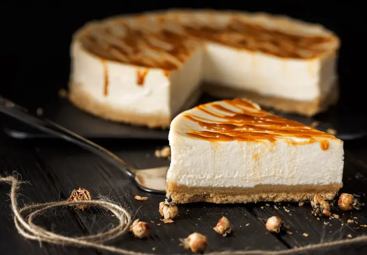Una fetta di cheesecake senza gelatina, con caramello colante, su un tavolo di legno scuro.