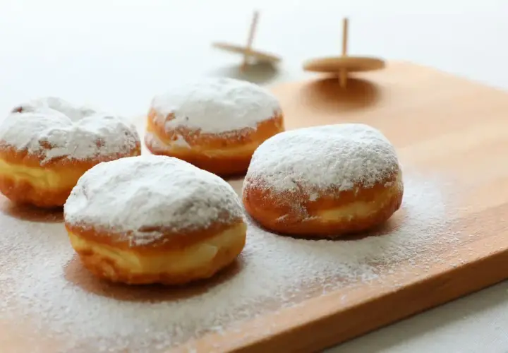 Quattro soffici bomboloni alla crema, cosparsi di zucchero a velo, invitano a un dolce momento.
