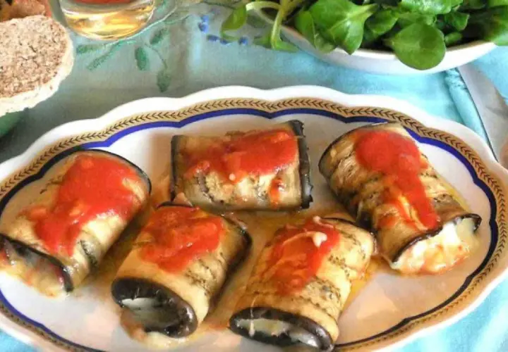 Deliziosi involtini di melanzane ripieni, conditi con sugo di pomodoro, su un piatto decorato.