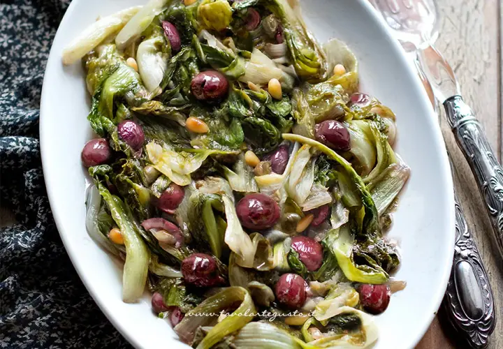 Scarola in padella con olive nere e pinoli, un contorno saporito e colorato, pronto per essere gustato.