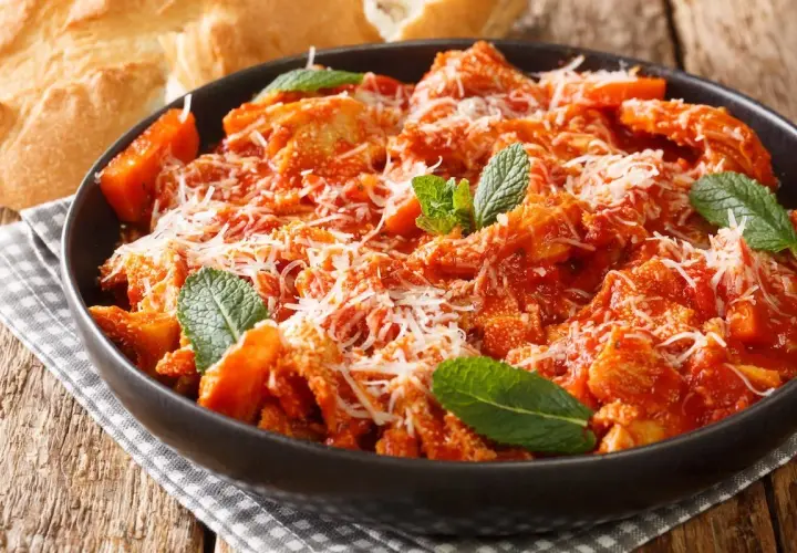 Trippa alla romana, la ricetta della nonna, servita in una ciotola scura con parmigiano e menta. Accanto, pane casereccio.