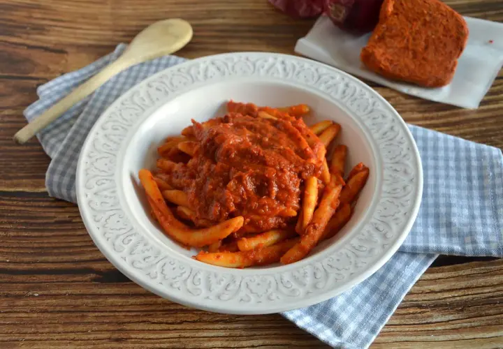 Piatto di pasta con sugo rosso piccante, condita con nduja calabrese. Accanto, un pezzo di nduja e cipolla rossa.
