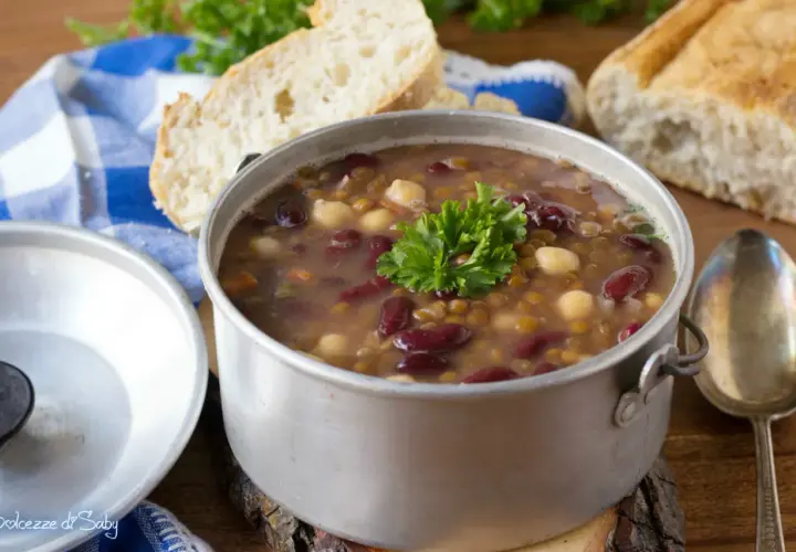 Una fumante zuppa di legumi, ricca di fagioli rossi, lenticchie e ceci, guarnita con prezzemolo fresco, accanto a pane casereccio.