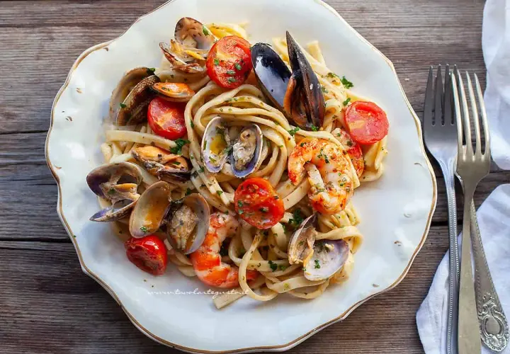 Un piatto invitante di scialatielli ai frutti di mare, con cozze, vongole e gamberi, guarnito con pomodorini e prezzemolo.