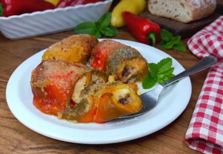 Deliziosi involtini di peperoni ripieni, dorati e succulenti, serviti su un piatto bianco con menta fresca.