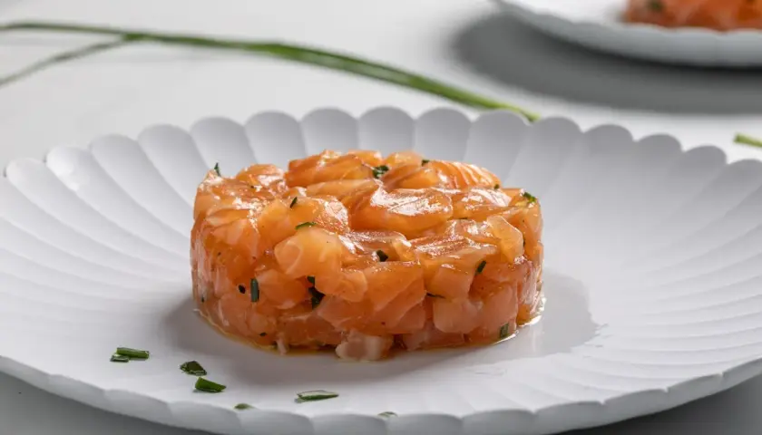 Tartare di salmone fresco, finemente tagliato e condito, servito su un piatto bianco con erba cipollina.