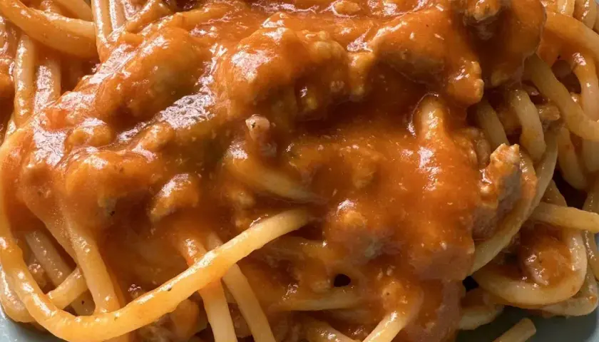 Un piatto di spaghetti al ragù, con un sugo ricco e saporito, dove spiccano i pomodorini.