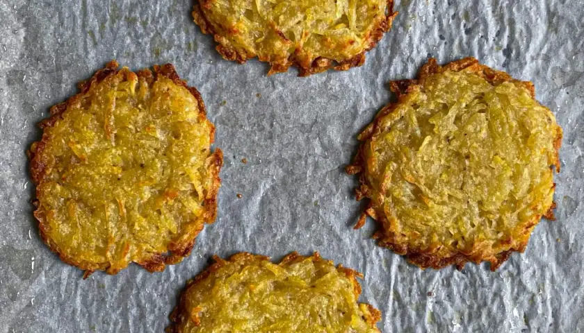 Quattro rosti di patate dorati e croccanti su carta da forno.