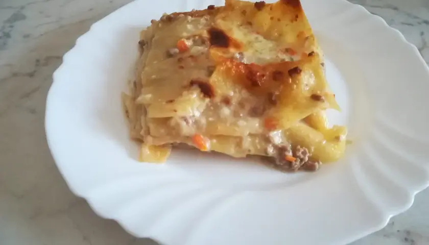 Porzione di lasagna classica, con strati di pasta, ragù e besciamella, servita su un piatto bianco.