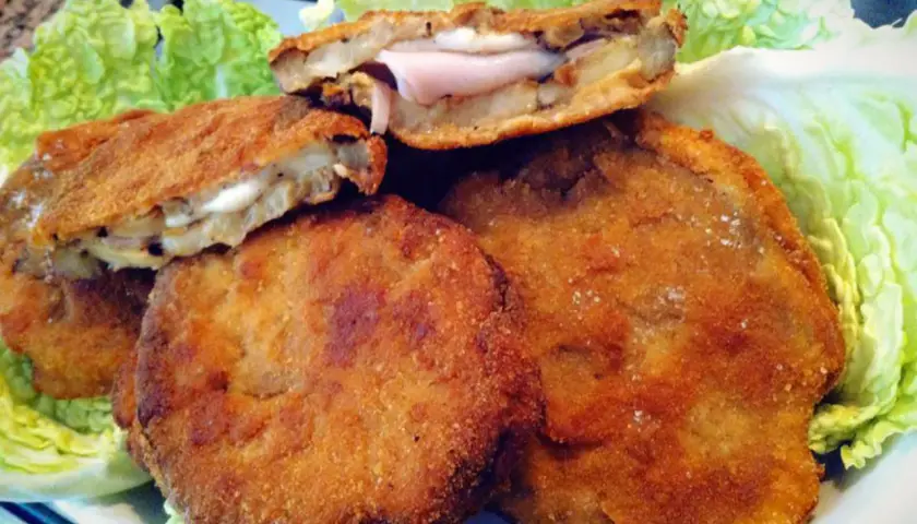 Cordon bleu di melanzane dorati e croccanti, ripieni di prosciutto e formaggio filante, serviti su un letto di lattuga fresca.