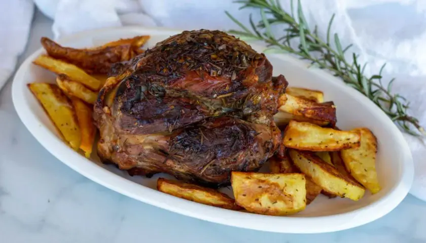 Stinco di maiale arrosto, dorato e succulento, servito con patate croccanti e rosmarino fresco.