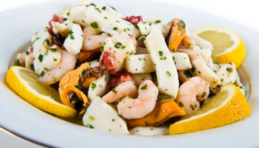 Deliziosa insalata di mare con gamberi, calamari, polpo e cozze, condita con prezzemolo e limone.