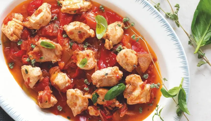 Piatto di coniglio alla cacciatora ricetta della nonna, con pezzi di carne tenera in salsa di pomodoro e peperoni, guarnito con basilico fresco e timo.