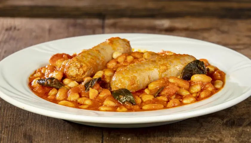 Salsiccia e fagioli in umido, un piatto rustico e saporito, servito su un piatto bianco.
