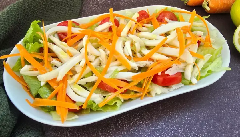 Deliziosa insalata di seppie con lattuga croccante, carote julienne e pomodorini freschi. Un piatto leggero e saporito.