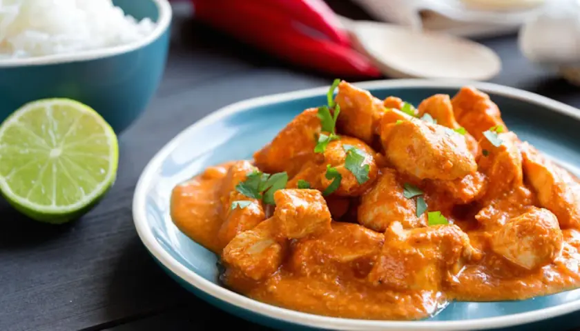 Bocconcini di pollo in salsa cremosa, guarniti con prezzemolo fresco, accompagnati da riso bianco e spicchio di lime.