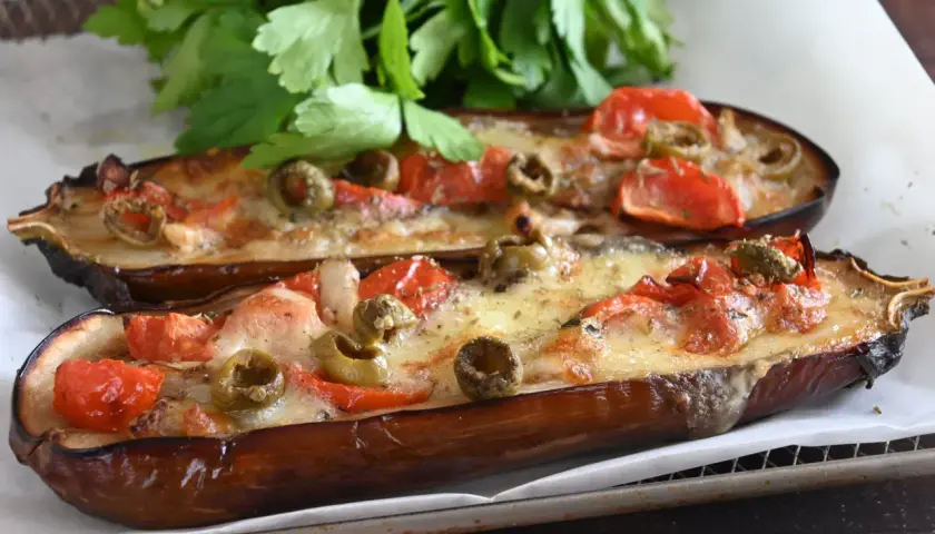 Melanzane alla pizzaiola, gustose e filanti, con pomodoro, olive e formaggio fuso, guarnite con prezzemolo fresco.