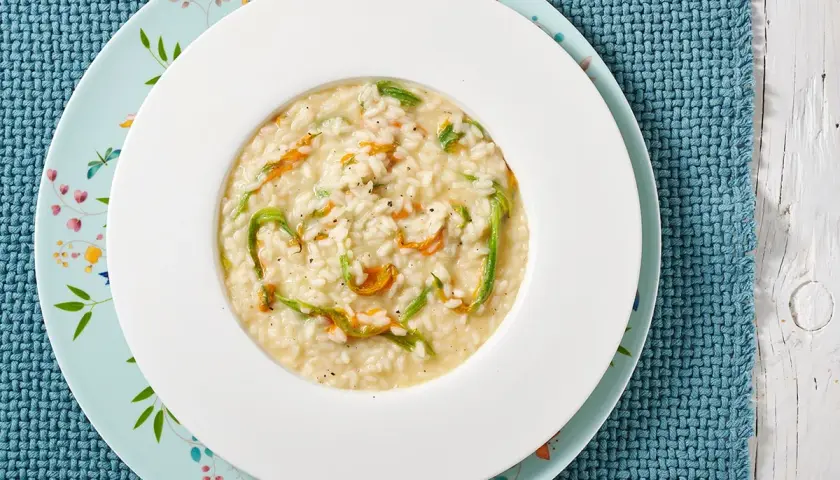 Un piatto di risotto ai fiori di zucca cremoso, con petali arancioni e fili verdi che si intrecciano nel riso bianco.