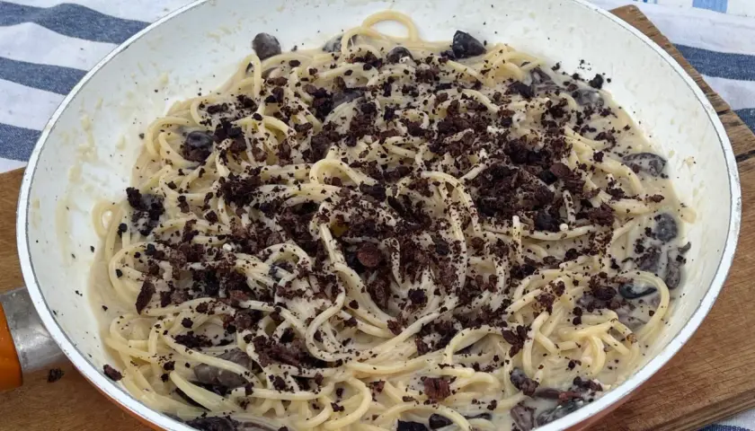 Spaghetti cremosi con olive nere e una spolverata di briciole scure, un'interpretazione audace della pasta alla cenere.