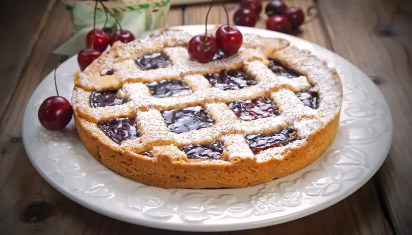 Deliziosa crostata senza burro con marmellata di ciliegie, cosparsa di zucchero a velo e decorata con ciliegie fresche.