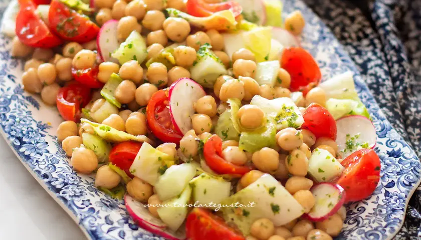 Un'insalata di ceci fresca e colorata con pomodorini, cetrioli e ravanelli, condita con erbe aromatiche.