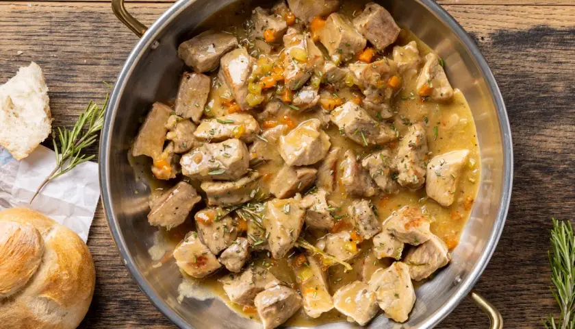 Un saporito spezzatino di vitello in umido, con carote e rosmarino, servito in una padella di metallo su un tavolo di legno.