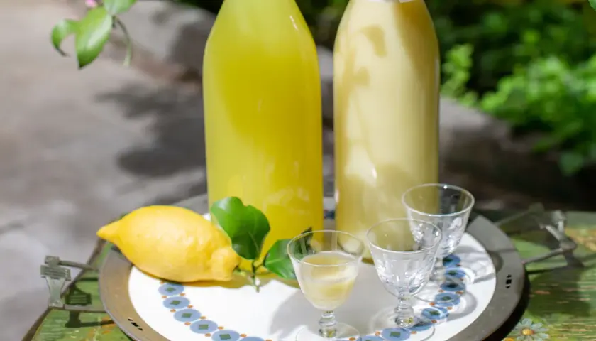 Due bottiglie di limoncello, una chiara e una cremosa, con limone fresco e bicchierini pronti per un assaggio.