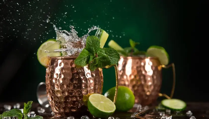 Moscow Mule ricetta: due tazze di rame con schizzi d'acqua, lime, menta e cetriolo. Fresco e dissetante.